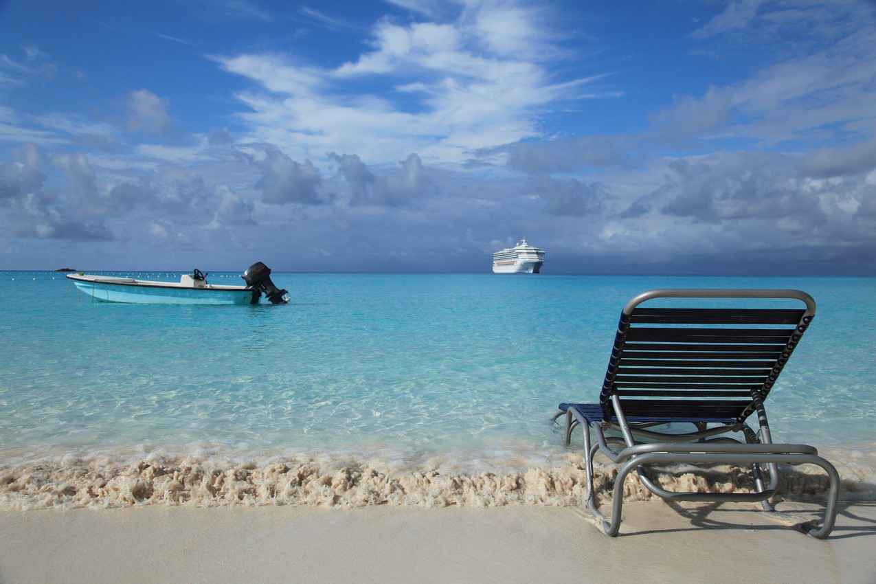 A Caribbean beach with a fishing boat and a cruise ship in the background.