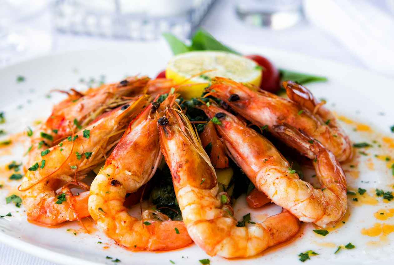 A plate full of decorative cooked shrimp with lemon in the center and seasoning on top.
