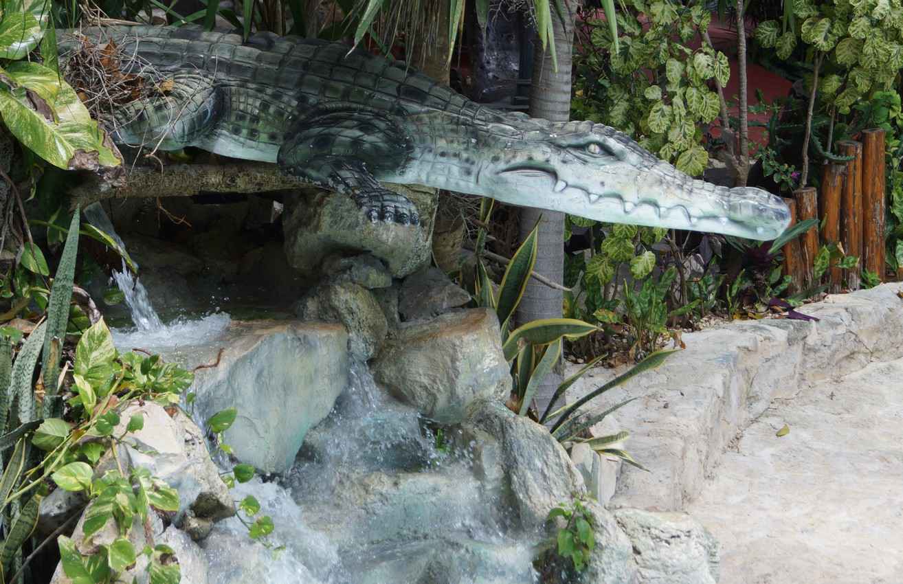 A glass alligator above a waterfall that is outside a restaurant.