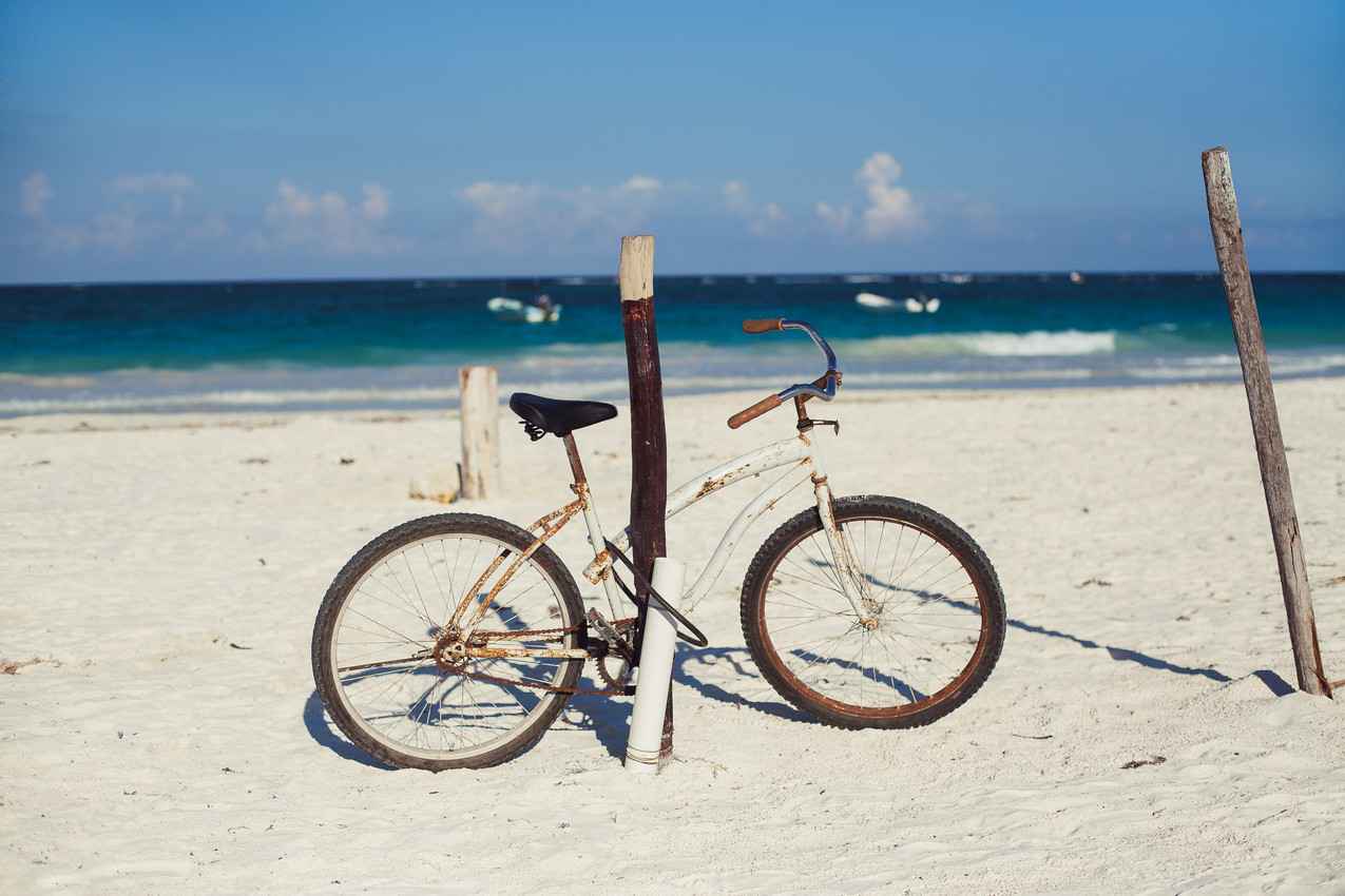 An old and rusty bike that is chained to a wooden post on the beach.
