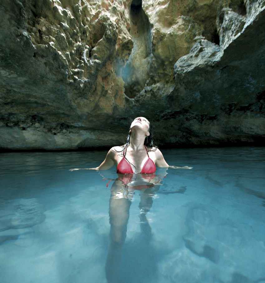 A super hot woman in a red bikini looking into the air from inside a cenote.