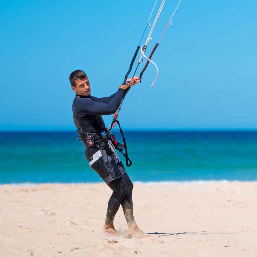A man standing on a Playa Del Carmen beach testing his kite board.