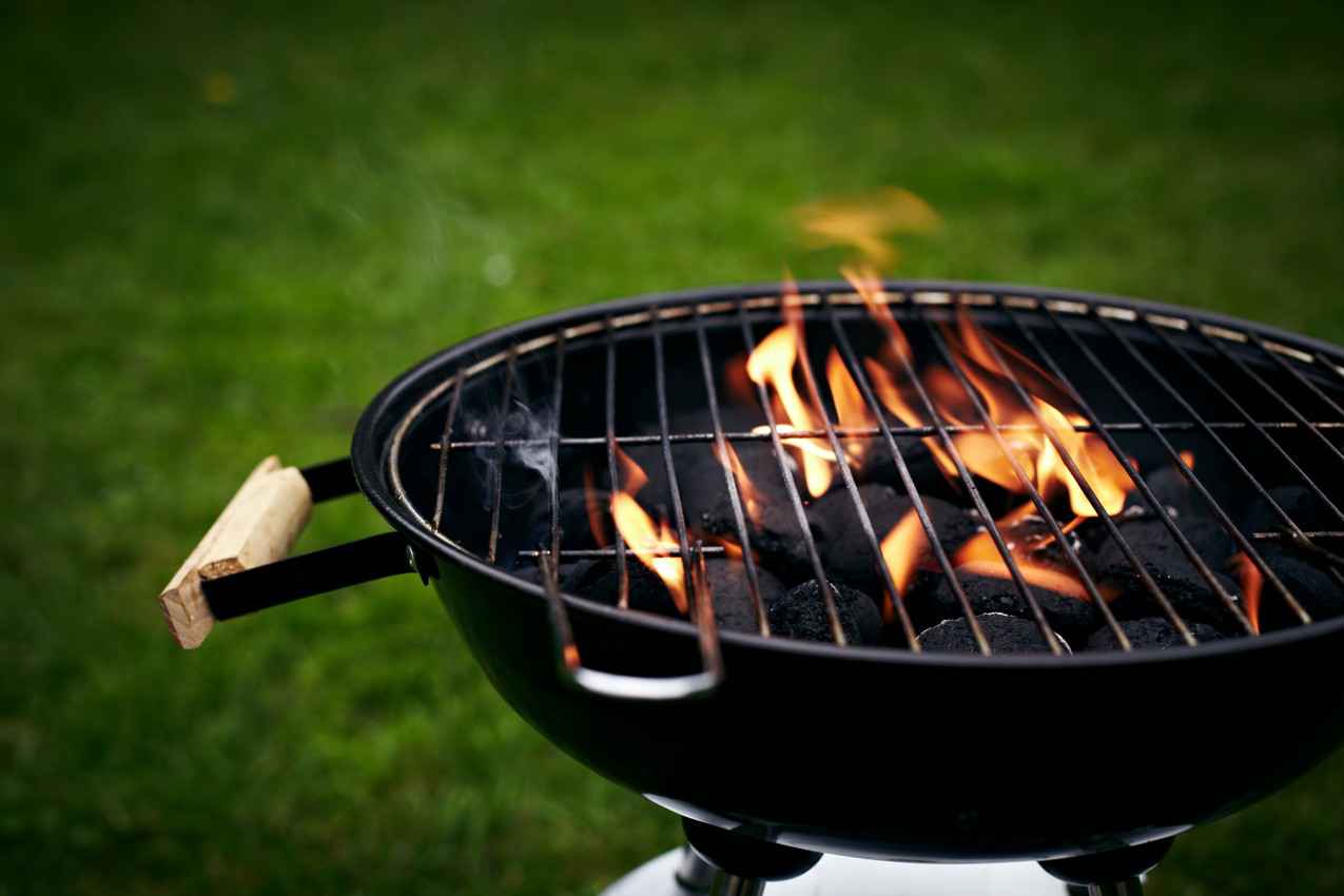 A charcoal grill burning with a large flame in a grassy backyard.