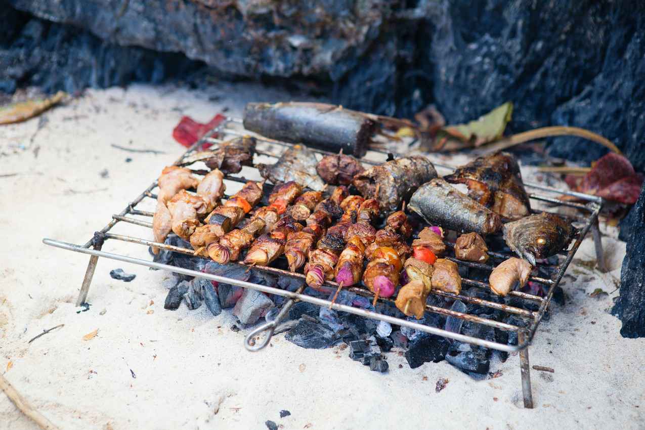 Fish and several kebabs cooking on an open air charcoal grill.