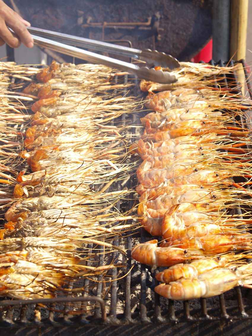 Several large shrimp cooking on a charcoal grill.