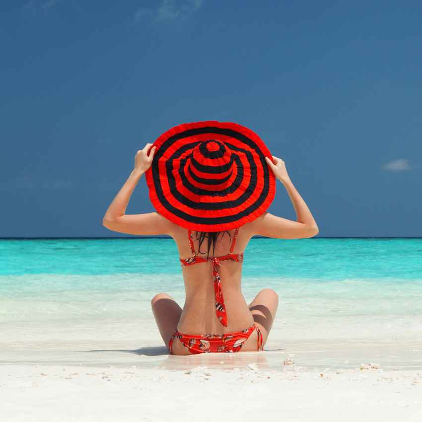 A very sexy woman on the Playa Del Carmen beach with a large red hat and a red bikini.