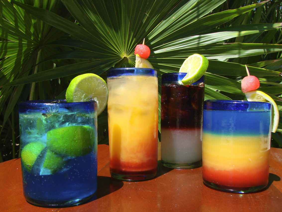 Several cocktails on a table with a jungle in the background.
