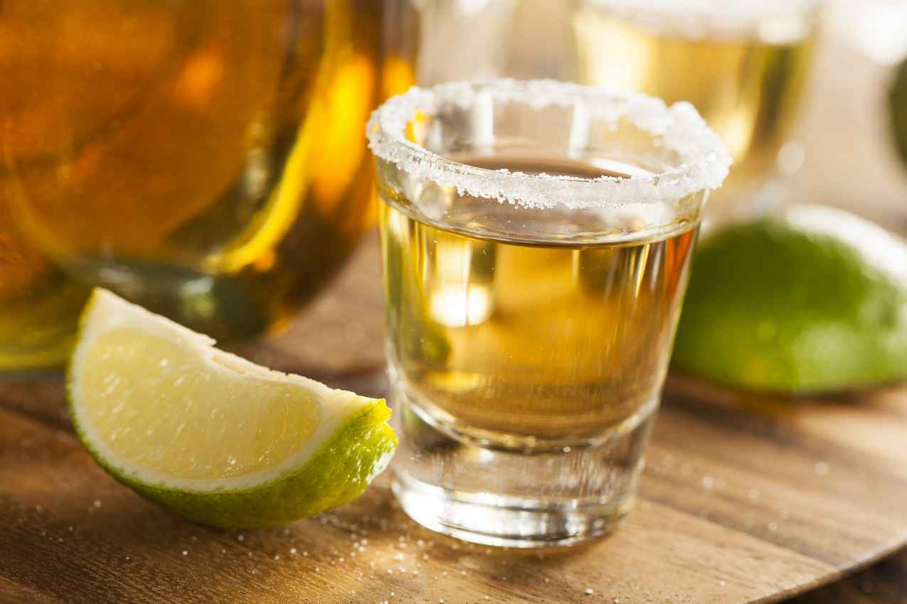 A tequila shot with salt around the rim and limes on its sides.