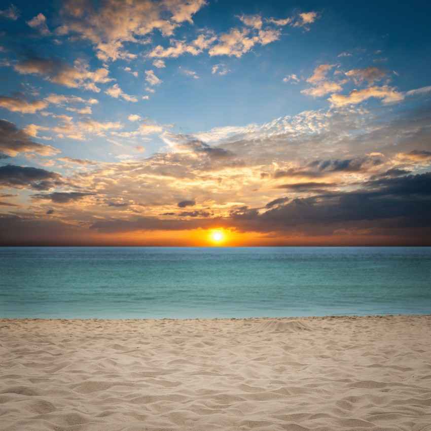 A great sunrise with orange clouds above the beach and clear blue water with white sand.