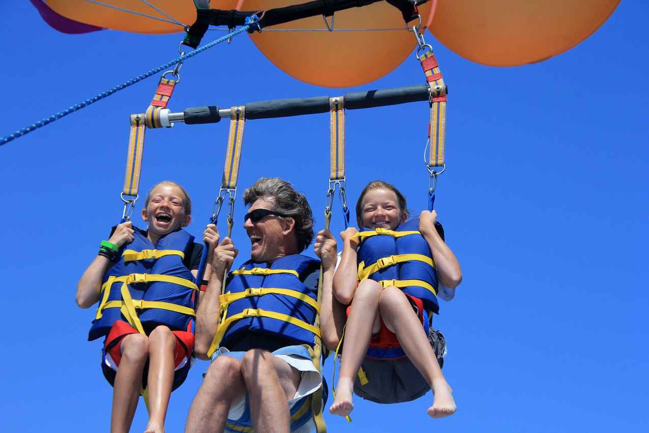 A father and two twin daughters parasailing together.