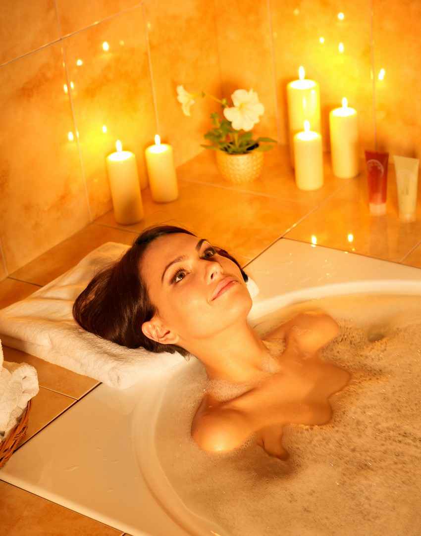 A woman sitting in a bubble bath Jacuzzi with candles all around her.