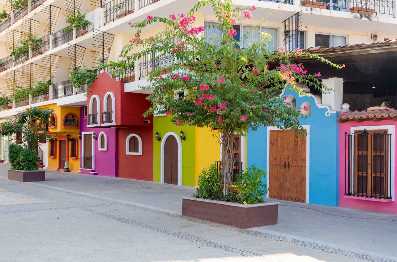 Several colorful condominiums near a Playa Del Carmen sidewalk and street.