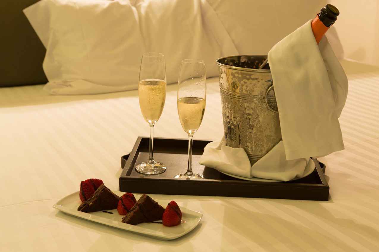 Two glasses of champagne near a chocolate and strawberry dessert on a bed in a Playa Del Carmen resort.