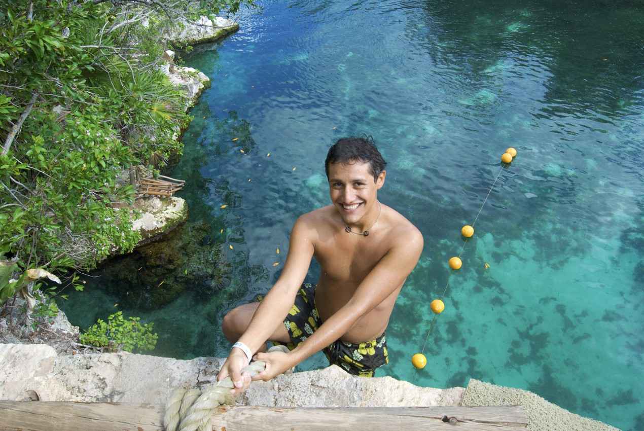 A young man climbing out of a cenote using a rope.