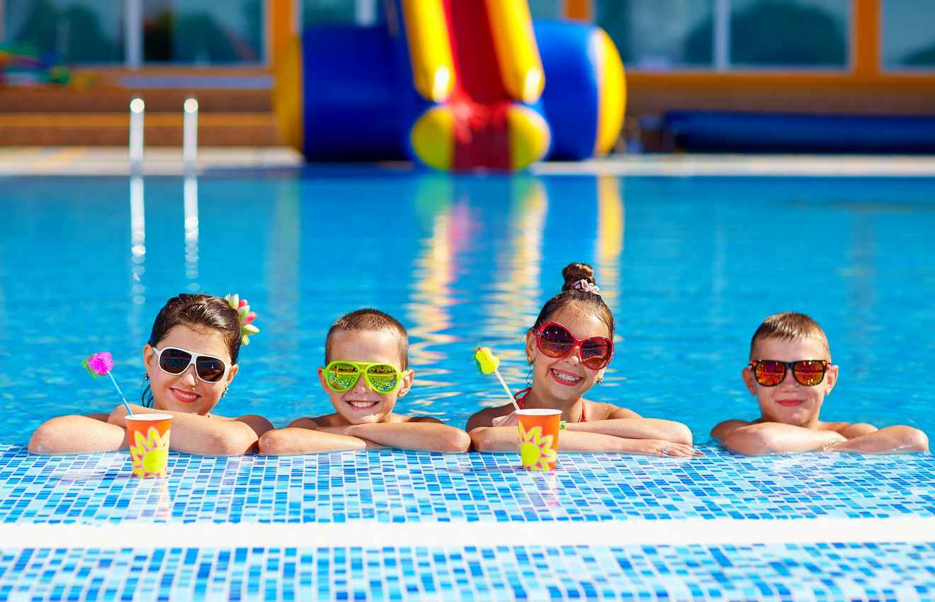 Four children with sunglasses and drinks in a swimming pool.