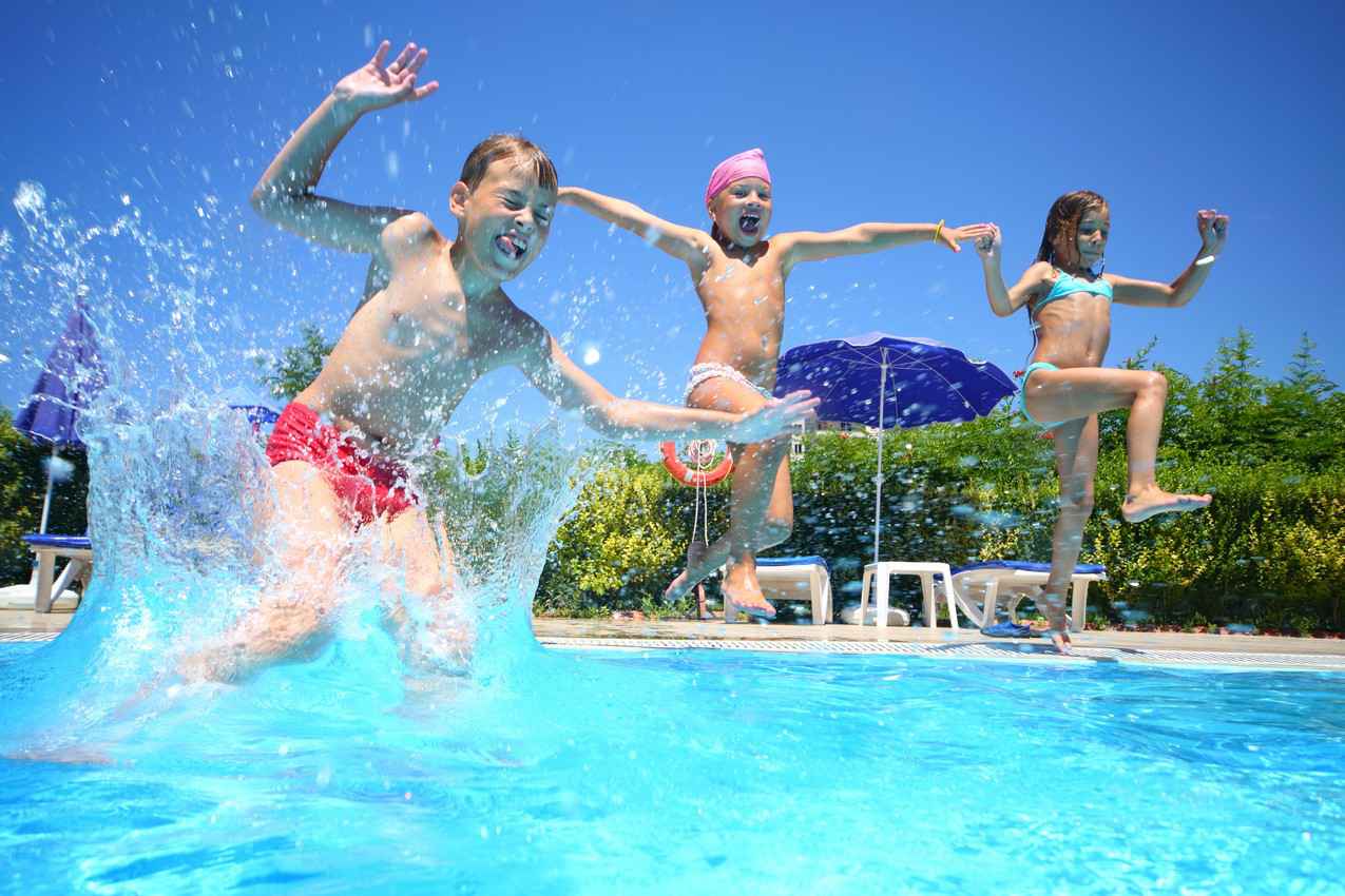 Three children jumping into a swimming pool.