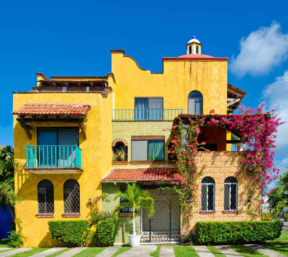 A beautiful yellow house in Playa Del Carmen that is surrounded by obviously well-kept plants.