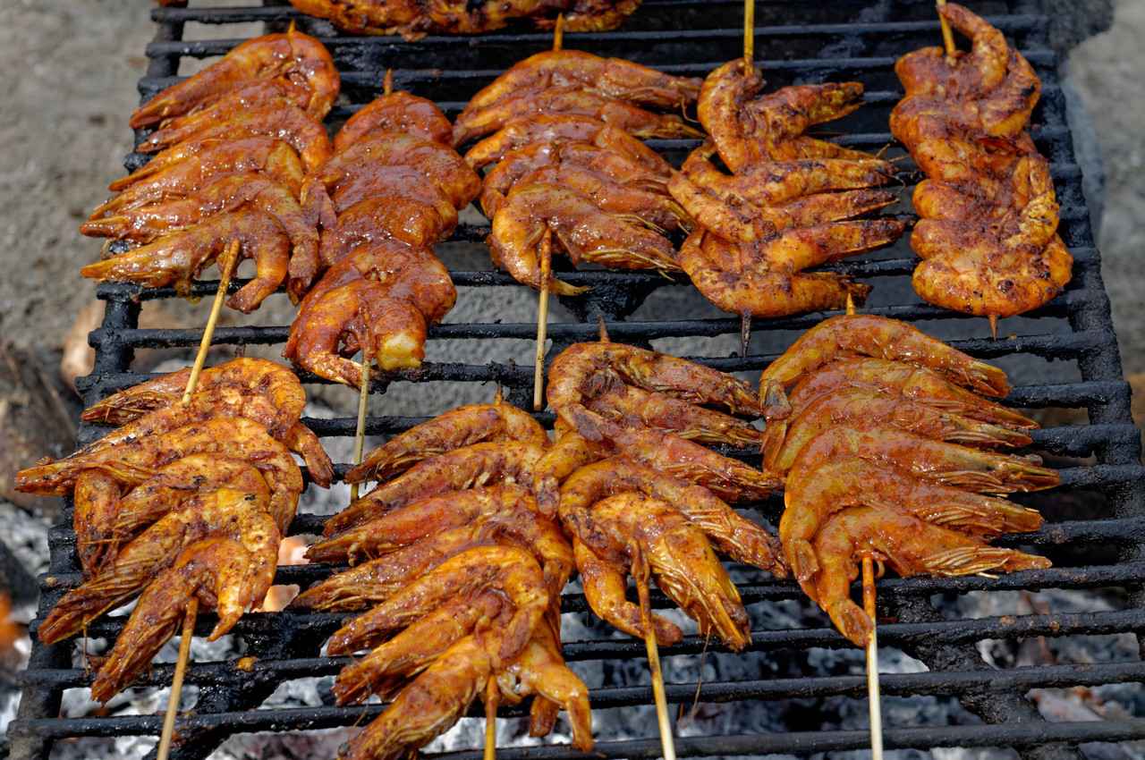 Heavily seasoned shrimp on skewers cooking over a charcoal grill.