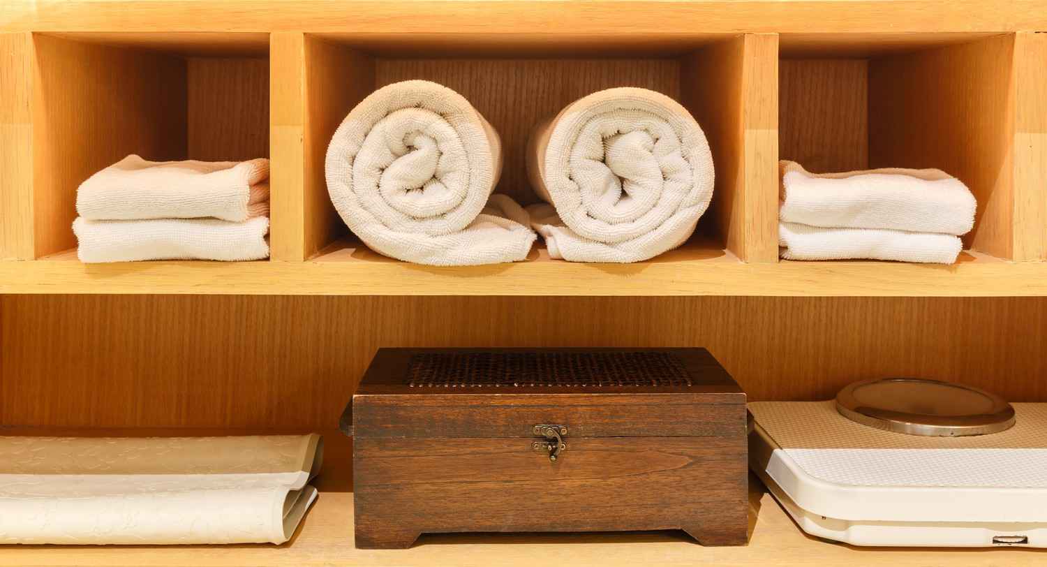 A closet in a resort that features large and small towels with a scale and a storage box.