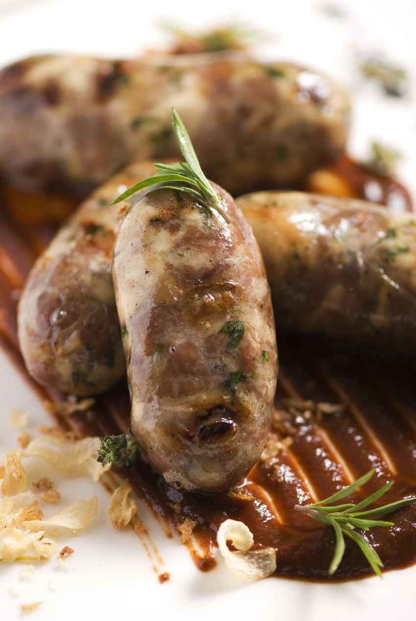 Several Italian sausages on a plate with gravy.