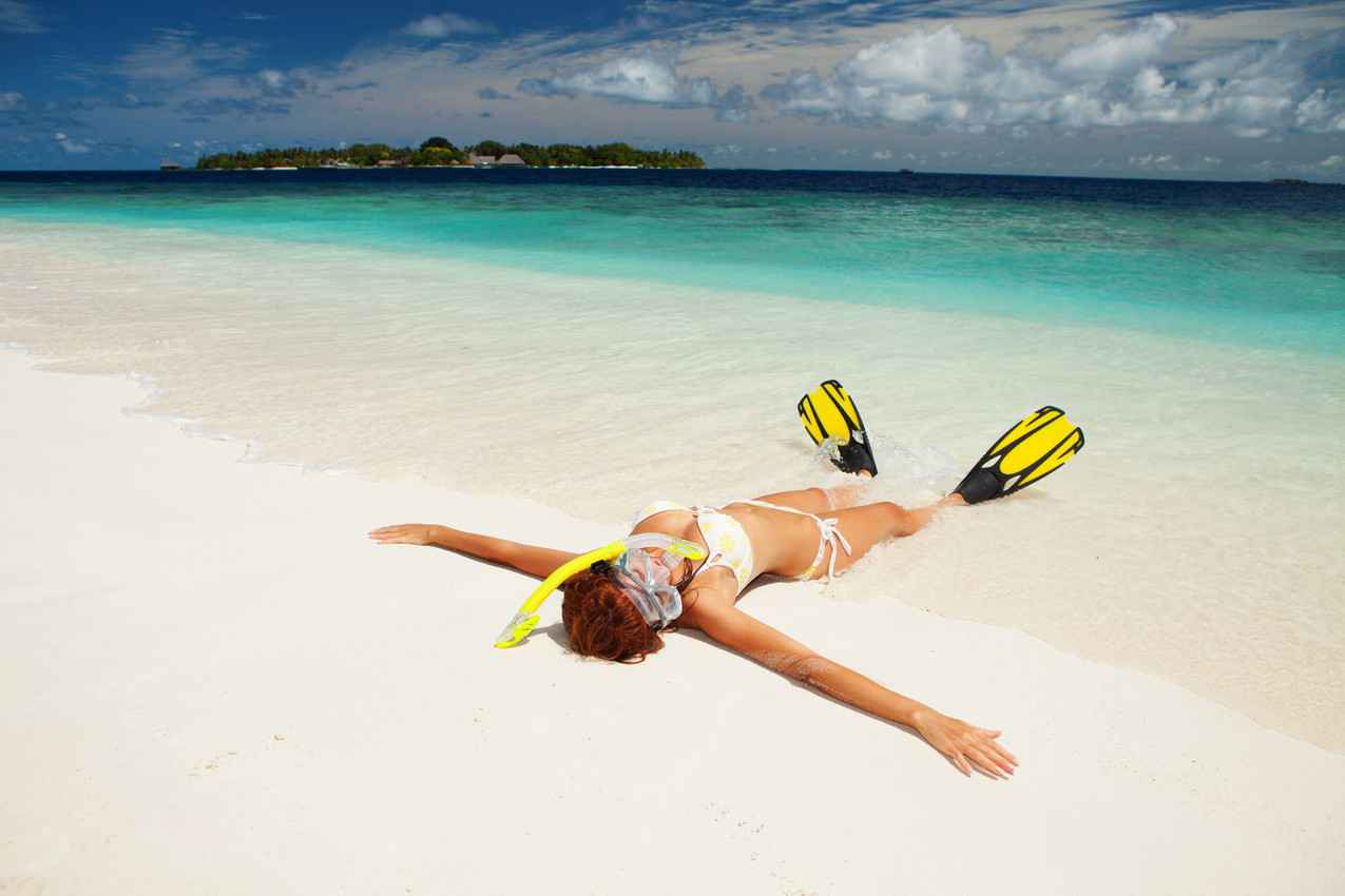 A woman with big boobs, a snorkeling mask, and fins is lying on the beach near Cozumel Island.