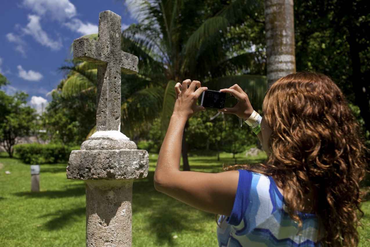 A woman taking a close-up photograph of a Christian cross at a Mexican cemetery.