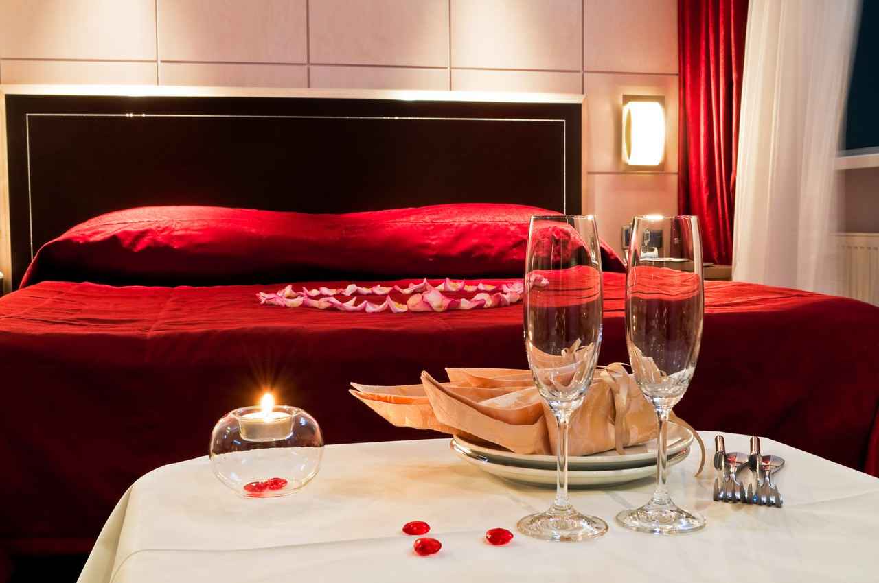 A sexy and romantic resort bed with heart flower petals and several champagne glasses.