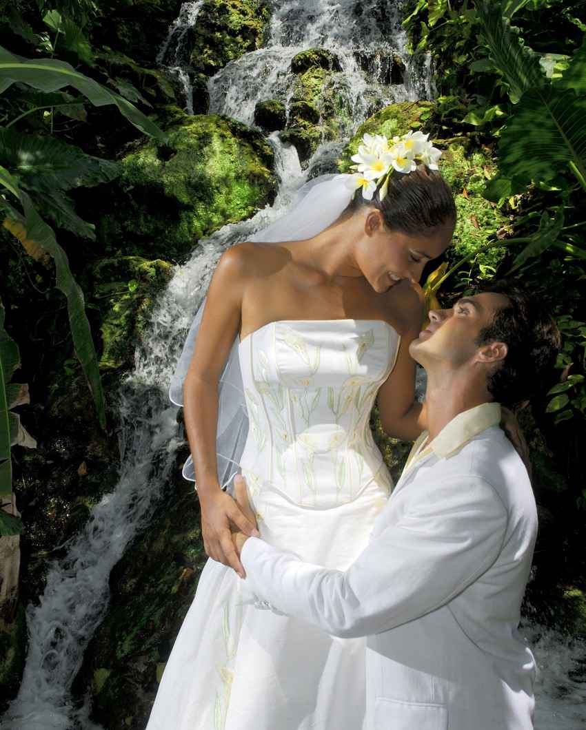 A bride and groom photo taken in the jungle near a beautiful waterfall.