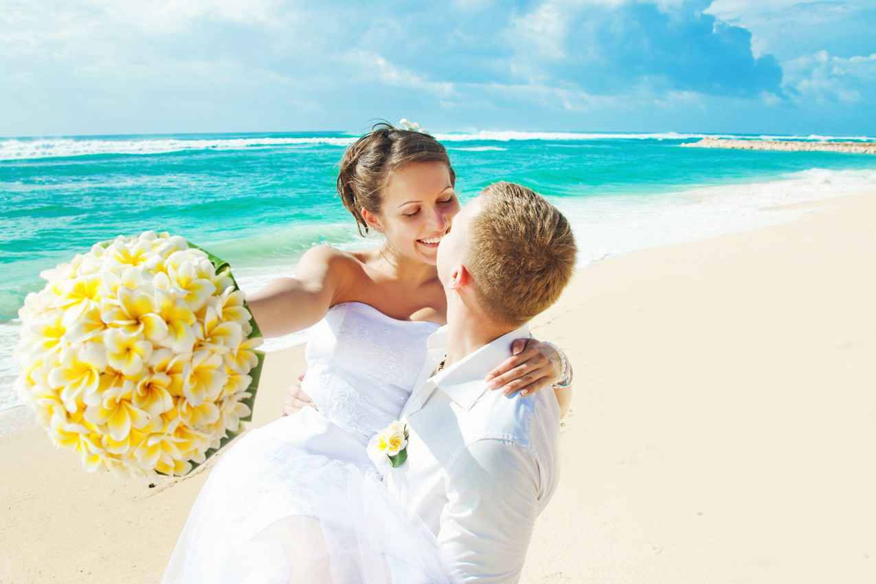 A wedding couple on the beach with the woman holding a bouquet.