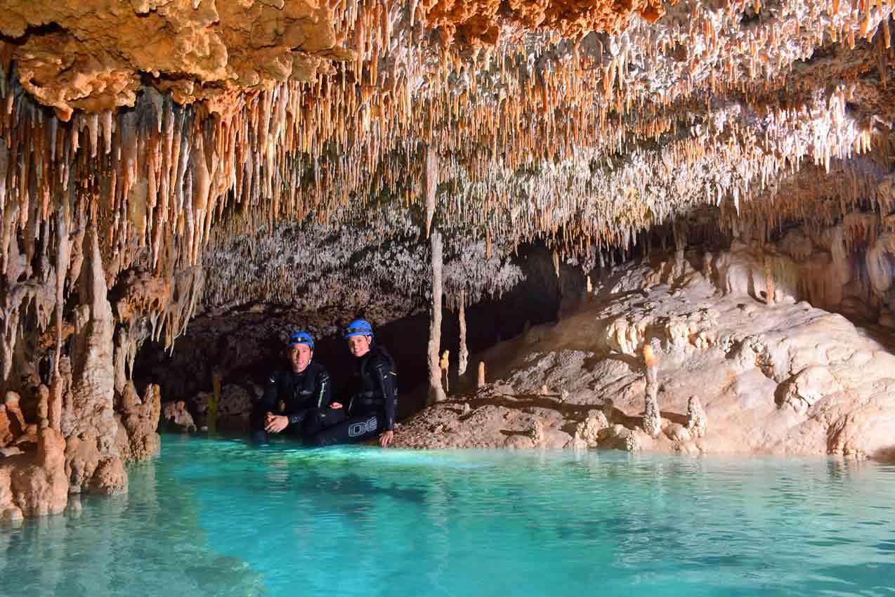 man-and-woman-sitting-on-edge-of-rio-secreto-cancun-cavern-pool-surrounded-by-interesting-rock-formations