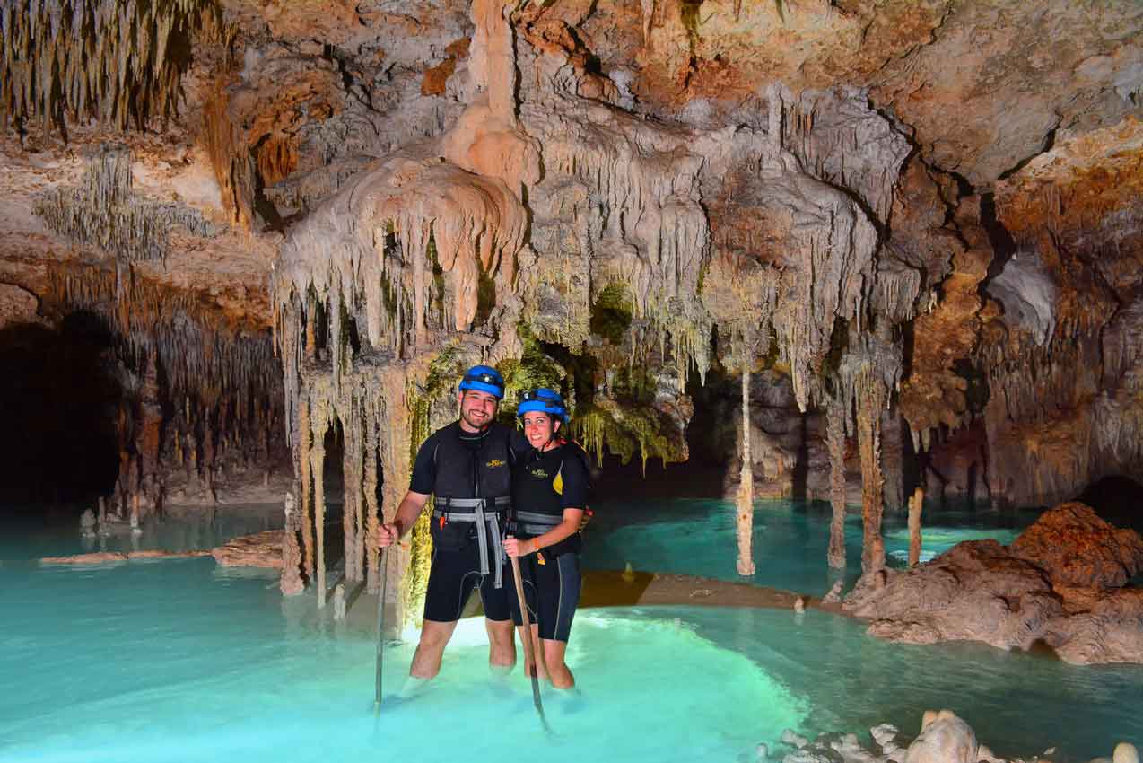 two-tourists-ankle-deep-in-clear-blue-water-holding-hiking-sticks-while-on-rio-secreto-tour