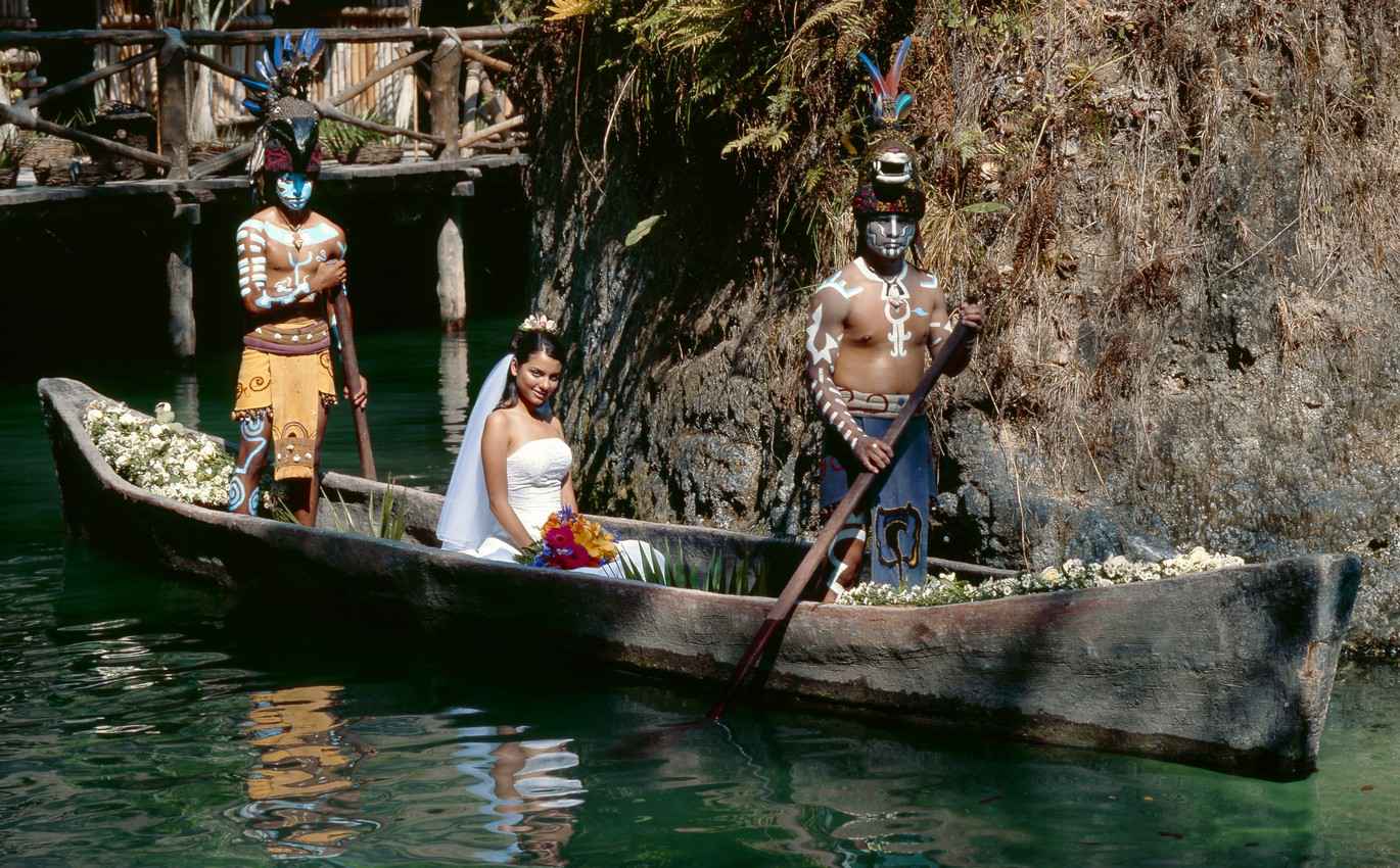 A bride being carried in a canoe by Mayan warriors.