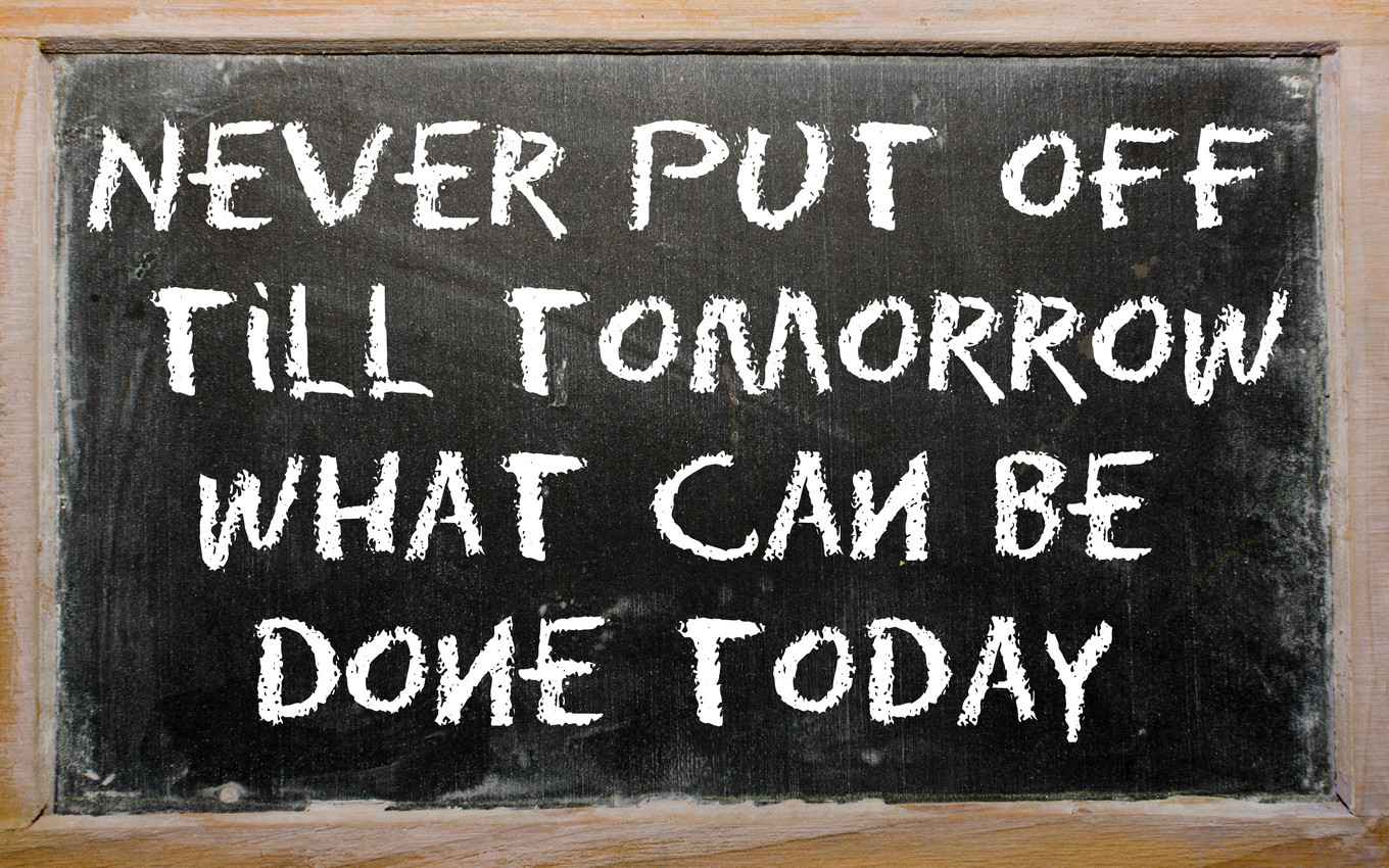The words, never put off till tomorrow what can be done today, written on a chalkboard.