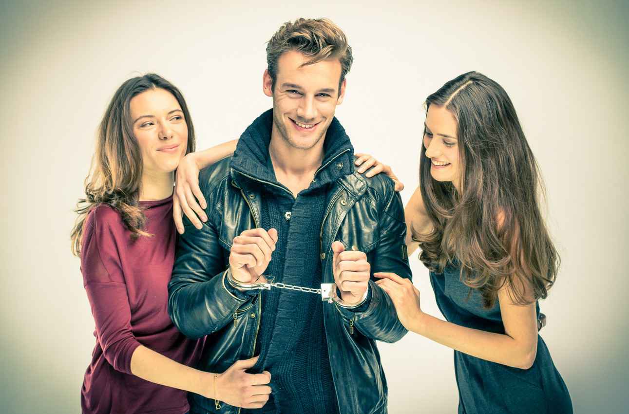 A cool guy wearing handcuffs with two beautiful women standing on each side of him.