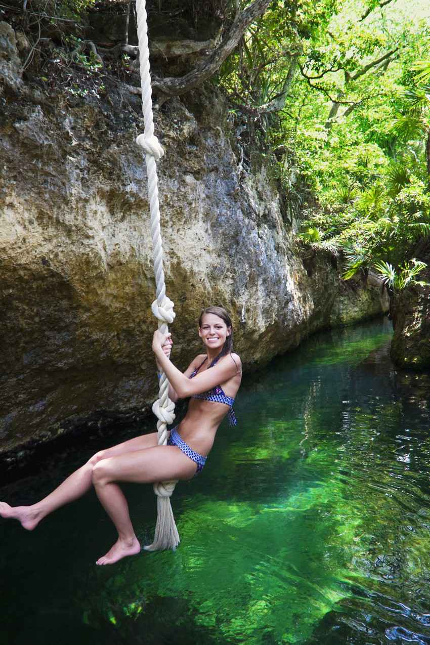 A young woman swinging on a rope swing above a cenote.