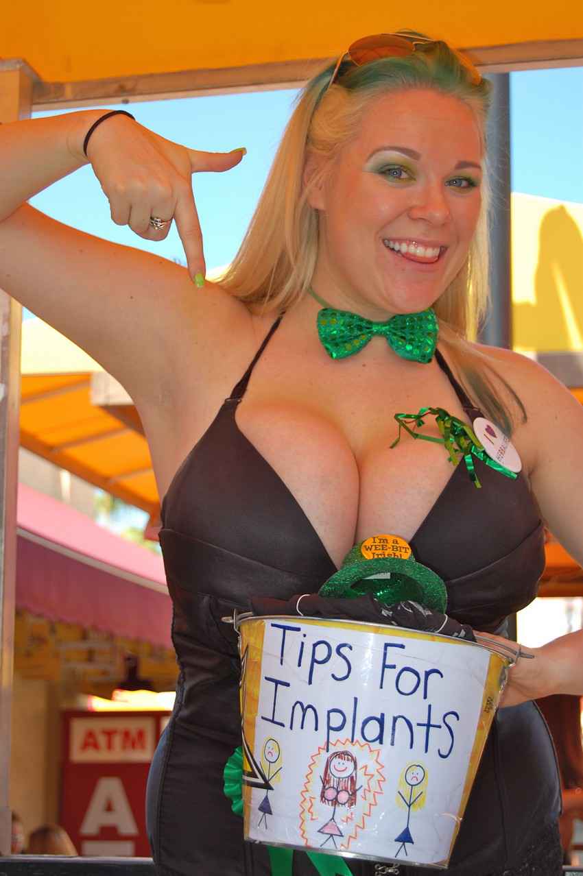 A woman with big boobs holding a sign that says, tips for implants tip jar.