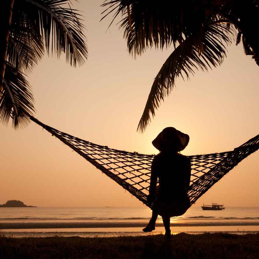 A woman sitting in a hammock with the beach in the background.