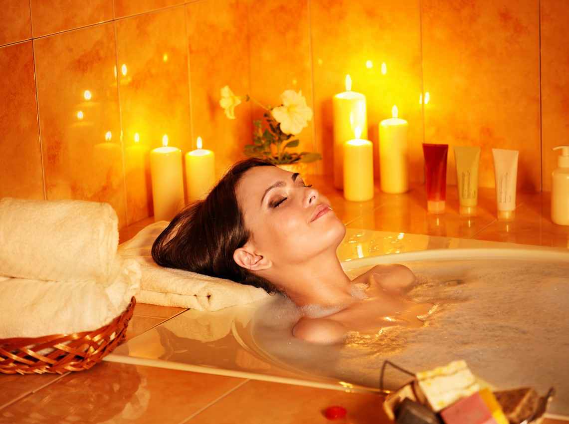 A pretty woman taking a candlelit bath at an exclusive resort.