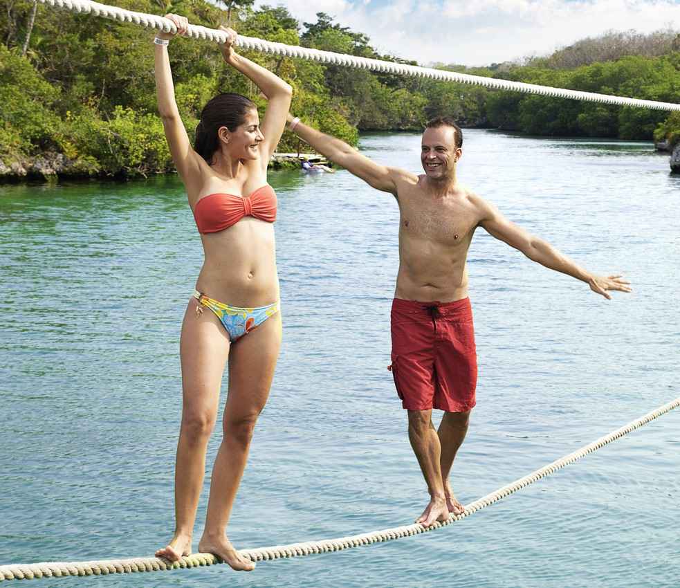 A man and a woman walking along a double rope line above the water.