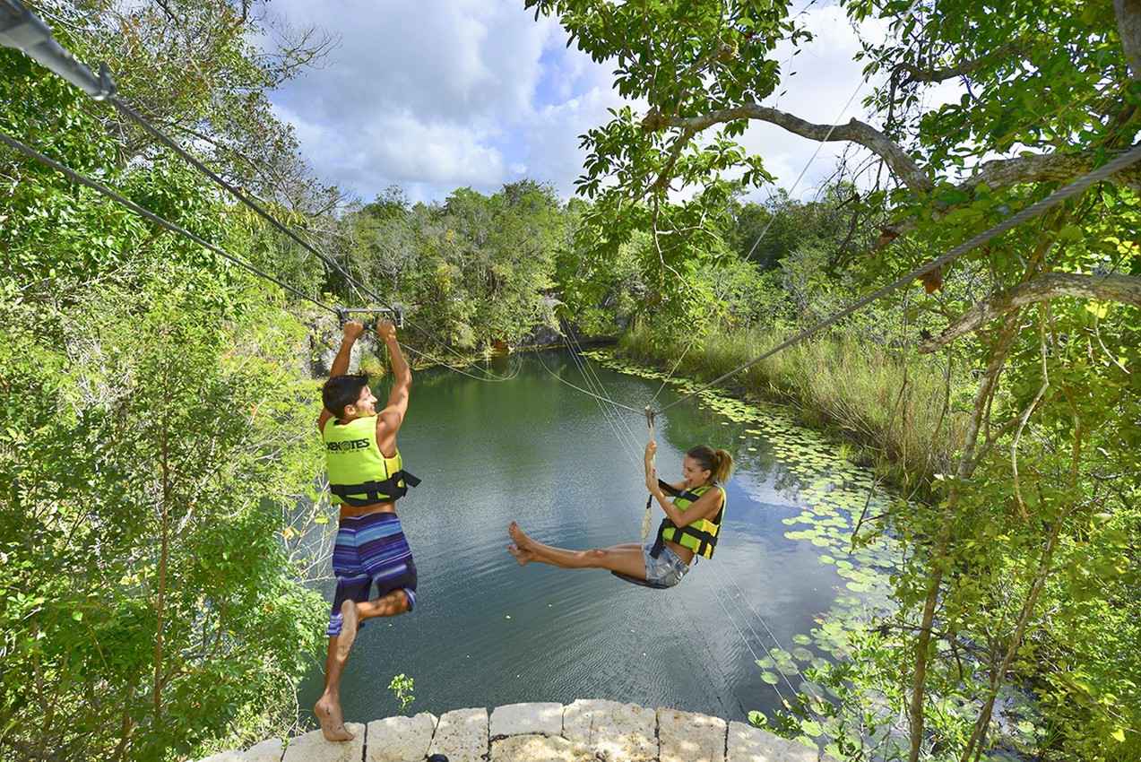 Two kids playing on a zip line near a cenote.