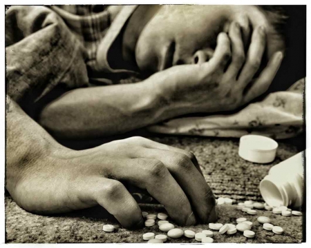 A black and white picture of a man lying on the floor with sleeping pills next to him.