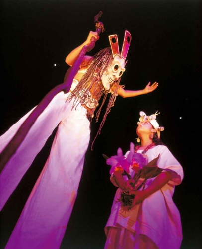 A man wearing an ancient Mayan costume on stilts and a woman holding flowers.