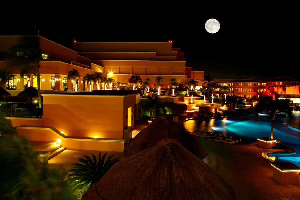 A full moon visible above a beautiful resort pool.