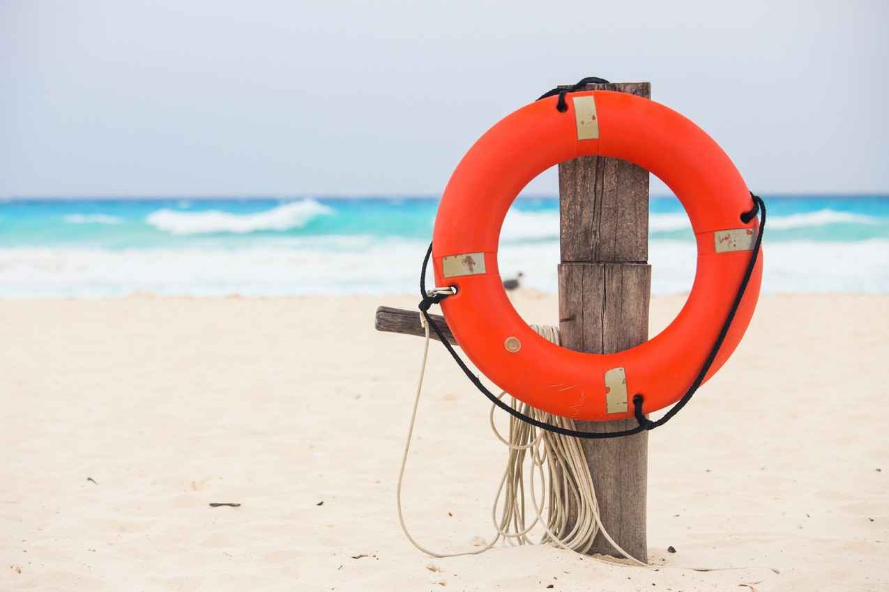 A white sand beach with a post holding an orange life preserver and a rope.