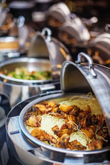 Several stainless steel pots holding dinner entrees at an all-you-can-eat resort buffet.