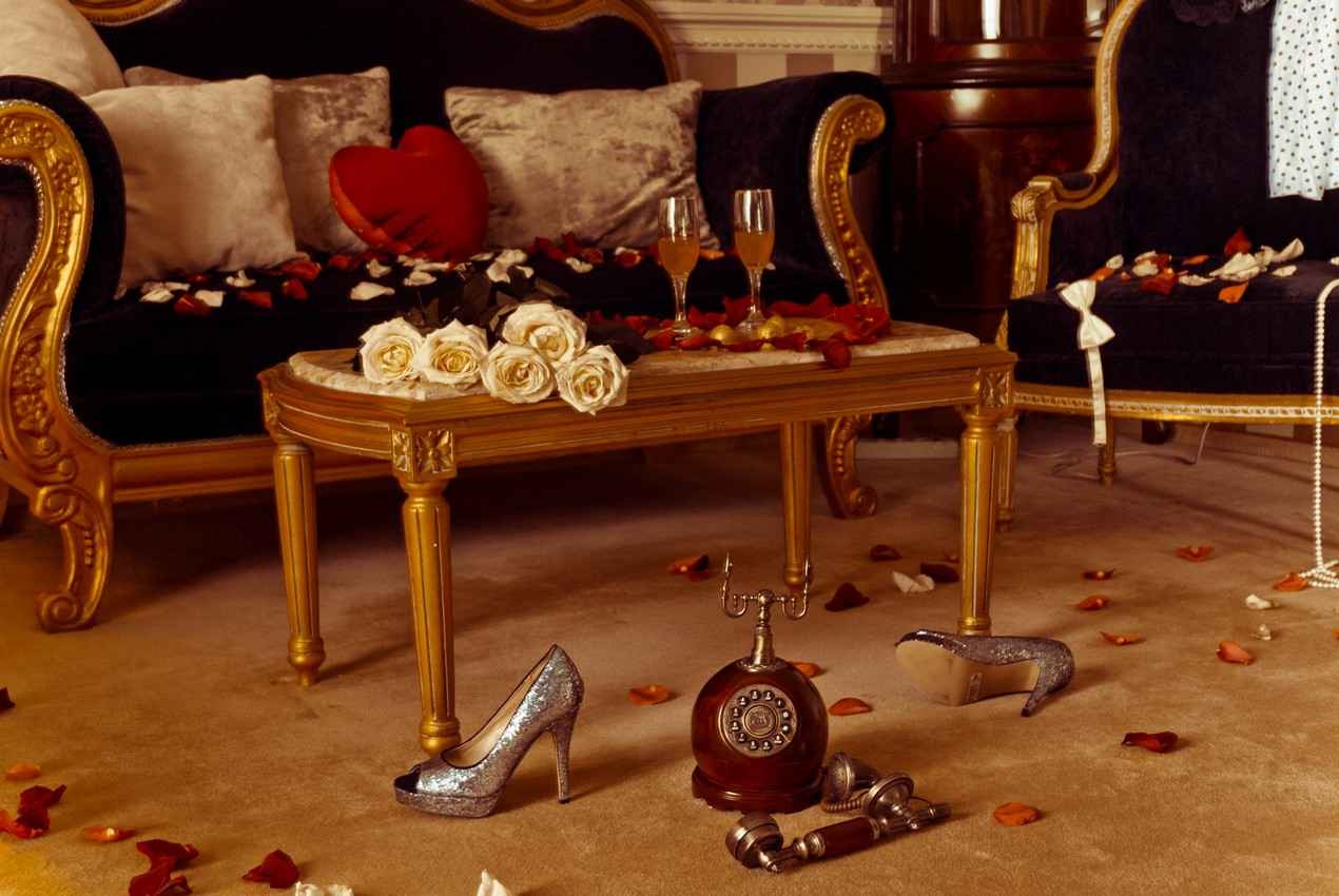 Flower petals strewn all around a room with champagne glasses in preparation for a romantic evening.