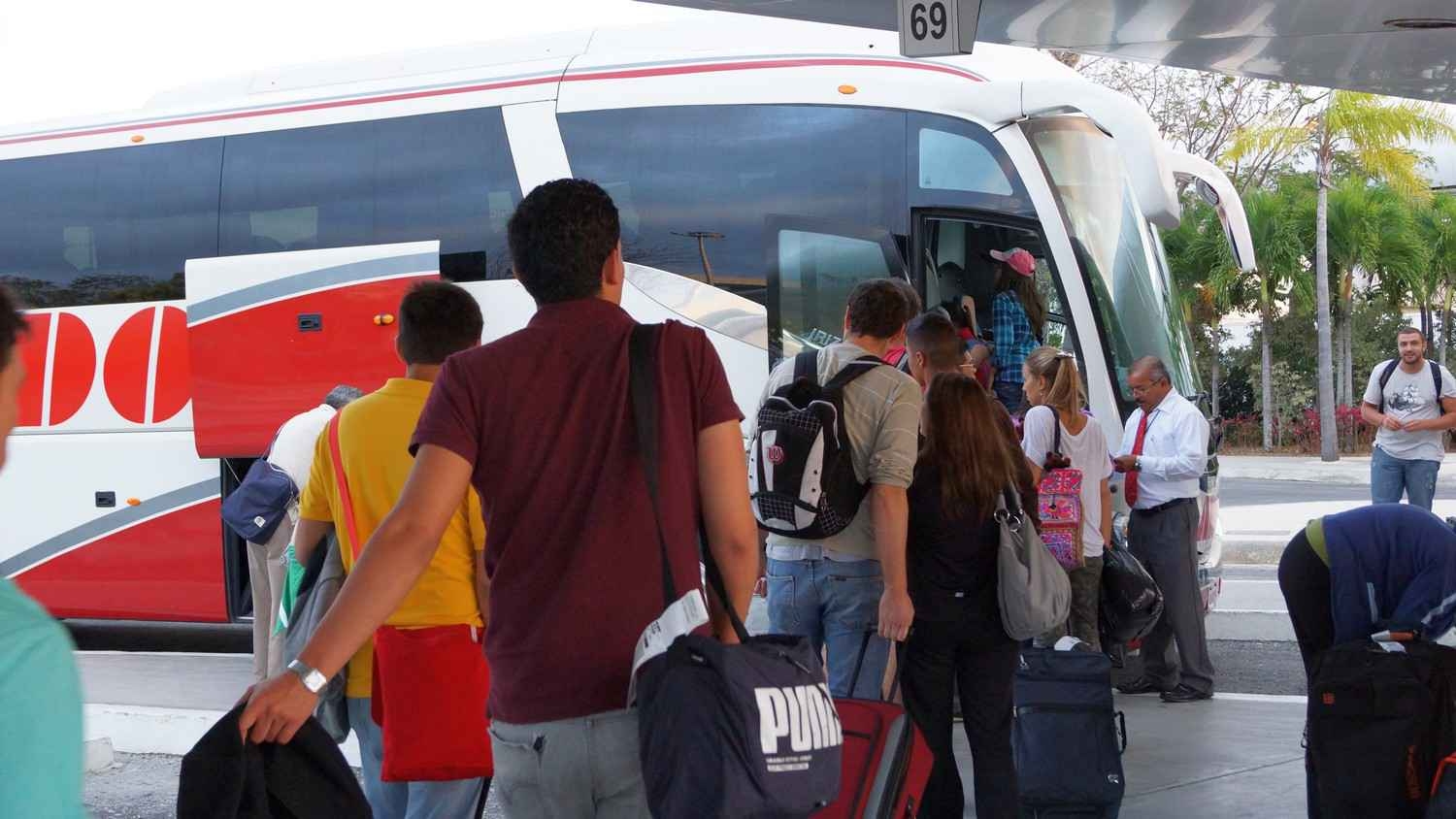 Several people boarding a transfer bus at the Cancun international Airport.