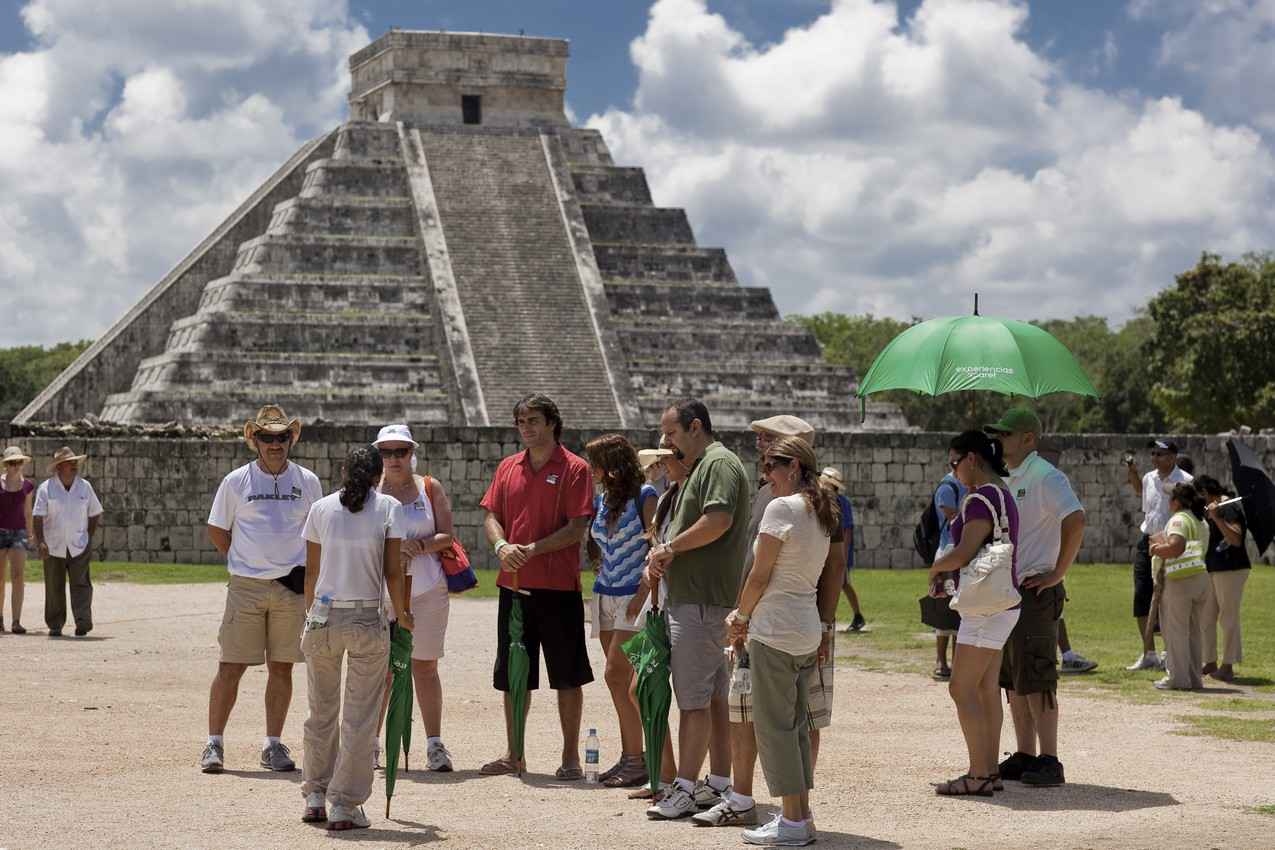 A group of tourists and a tour guide gathered in front of El Castillo pyramid.
