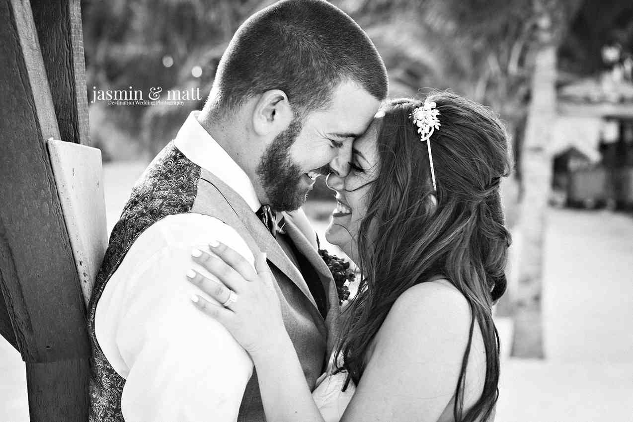 A black and white picture of a bride and groom kissing near some trees.
