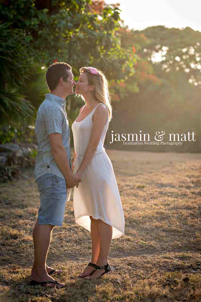 A couple kissing in front of a forest with sun shining on them.